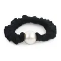 Détail d'un chouchou en satin noir avec perle blanche centrale pour coiffure élégante. - Noir