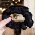 Black velvet scrunchie detail view showcasing the soft ruffled fabric texture close up. - Black