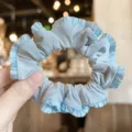 Close-up of light blue satin hair scrunchie with cute ruffled edge detail for daily wear. - Blue