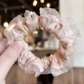 Détail en gros plan du chouchou rose pastel en dentelle plissée, texture douce et style chic. - Rose