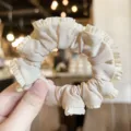 Detailed close-up of a elegant beige satin ruffled hair scrunchie, soft fabric texture. - Milk Tea