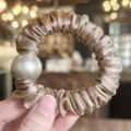 Close-up of elegant satin hair scrunchie featuring a large pearl detail, soft fabric texture. - Light Coffee