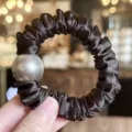 Close-up detail of black satin hair scrunchie with large grey pearl, elegant elastic hair tie. - Dark Brown