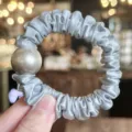 Close up detail of a light blue satin hair scrunchie featuring a large pearl ornament. - Blue