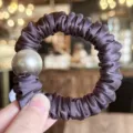 Close-up detail of dark gradient satin hair scrunchie featuring a large metallic bead. - Deep purple