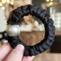 Detail view of a black satin hair scrunchie featuring a large elegant pearl decoration. - Black
