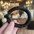 Gros plan détaillé de l'élastique à cheveux noir en satin avec deux grandes perles. - Noir