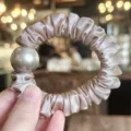 Detail shot of an elegant satin hair scrunchie with a large metallic bead for women. - Light Pink