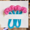 Detail view of colorful faceted star hair ties with blue elastic bands on a white card. - Rose Red
