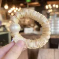Detailed view of champagne satin scrunchie with large pearl hair tie elegant hair accessory - M / Nude