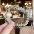 Detailed shot of a luxury satin scrunchie featuring an elegant large pearl charm in soft green. - M / Grey Green