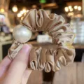 Close-up detail of golden satin hair scrunchie with large white faux pearl decoration. - L / Brown