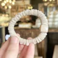 Detalle de coletero de pelo plisado beige con cuenta cuadrada, accesorio elástico. - Color Té con Leche