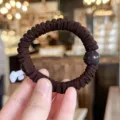 Detailed shot of dark brown pleated hair scrunchie with smooth round bead accessory. - L / Brown
