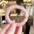 Close-up detail of the pink pleated hair scrunchie with a glossy bead design, soft texture. - L / Pink