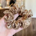 Gedetailleerd aanzicht van een luxe gouden satijnen haarscrunchie met gladde textuur. - S / Lichtkoffie