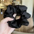 Black satin scrunchie hair tie detail view, soft fabric elastic ponytail holder accessory. - Black