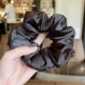 Dark brown satin scrunchie detail view, soft stuffed hair accessory closeup photography. - Brown
