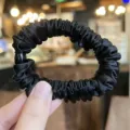 Close-up detail shot of black satin hair scrunchie showing smooth fabric texture and elastic design. - L / Black