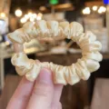 Close-up detail of the elegant satin scrunchie, soft fabric with high elasticity for hair. - L / Cream