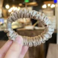 Detail view of a luxurious champagne satin hair scrunchie with cute grey bead accent. - L / Milk Tea