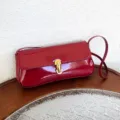 Detailed close-up of red patent leather underarm bag featuring a stylish gold lock closure. - Red