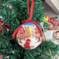 Nahaufnahme einer Weihnachtskugel am Baum mit winterlichem Dorf-Design und rotem Band. - Stil 14-15020