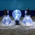 Detailed view of mini LED bulbs placed on sand surface, creative decorative lighting item. - Vintage Bulb Style