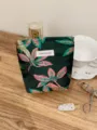 Detailed close-up view of the dark green leaf-patterned cosmetic pouch with brand tag. - S / Green Base Pink Floral Small
