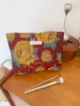 Close-up of vintage floral cosmetic pouch detail, showing woven fabric and brand label. - L / Red Base Gold Flower