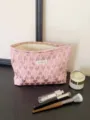 Detailed view of pink heart quilted cosmetic bag, portable makeup pouch shown on dark table. - L / Pink