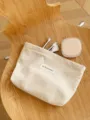 Detailed close-up of a beige corduroy cosmetic pouch placed on a wooden background with brushes. - Beige