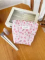 Floral makeup pouch detail showing pink pattern fabric and brand label on wooden table. - S / Pink Flower
