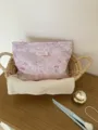 Close-up detail of the stylish floral cosmetic bag in a woven basket on a wooden table. - L / Purple Floral
