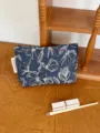 Detailed shot of a stylish blue floral cosmetic bag on a wooden surface with makeup tools. - M / Blue Floral