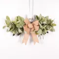 Artificial olive leaf wreath with burlap bow detail, perfect for wall hanging decor. - Olives