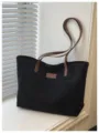 Detailed view of the black casual tote bag featuring brown straps and front logo patch. - Black without Pendant