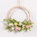Easter wooden bead wreath hanging detail showing colorful eggs, green leaves and white flowers. - 85980