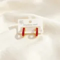 Primer plano de pendientes de aro dorados en U con piedras baguette rojas y acero inoxidable. - En Forma de U 7 Piedras