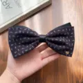 Gros plan d'un pince à cheveux nœud floral sombre avec satin noir et petit chien en métal doré. - Style Nœud Breloque Chien / Violet Floral