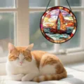 Close-up detail of the vibrant stained glass sailboat suncatcher hanging by a sunlit window. - Sunset Sailboat