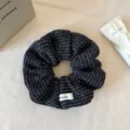 Close-up van een stijlvolle zwarte gebreide haarscrunchie met witte textuur en label. - Zwart