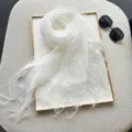 Close-up detail of a lightweight white silk scarf elegantly draped on a display tray. - Milky White