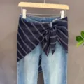 Detail view of denim jeans featuring a chic navy striped waist scarf wrap for trendy layers. - Black