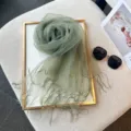 Close-up detail shot of sage green mesh fringe scarf styled on decorative board with props. - Green