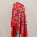 Detail view of a red embroidered floral shawl wrap with fringe, warm and festive style. - Red