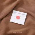 Gedetailleerde close-up van de roze ronde hijab magneet op witte kaart met bruine stof. - 1 Stuk/Verpakking / Roze