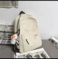 Detail view of minimalist beige backpack featuring front pocket, sturdy zippers, and cute duck charm. - Single Bag / White