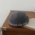 Nahaufnahme Detail des dunkelgrauen Baumwoll-Dockerhuts mit weißem Sticktext am Rand. - 48-50cm / Grau
