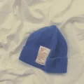 Primo piano dettagliato di un berretto in maglia blu con patch di testo bianco. - Bambini Blu Reale